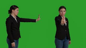 Close up of young manager showing stop talking sign with palm, expressing negative gesture and denial. Female worker in office suit doing rejection and refusal symbol over greenscreen backdrop. photo