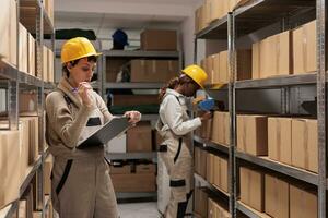 Warehouse operative looking at checklist on clipboard and counting goods boxes. Shipping company worker doing restock and checking inventory audit in distribution department stockroom photo