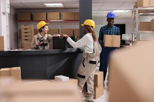 Smiling storehouse operators chatting at reception desk doing inventory. Post office storage workers managing dispatching and using barcode scanner on black box at counter photo