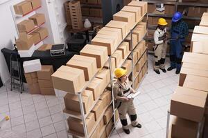 Diverse shipping service supervisors team working in warehouse, checking inventory system. Storehouse assistants reading stock supply report on clipboard and scanning parcels top view photo