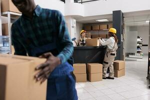 Delivery department warehouse coworkers taping parcel with adhesive at table. Mail sorting center employees closing cardboard box and carrying heavy container at post office storehouse photo