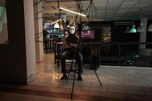 Hacker with mask threatening to expose important data on live broadcast, asking for ransomware late at night. Young masked thief hacking computer system and breaking into online server. photo