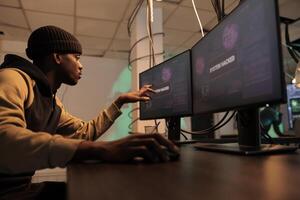 African american hacker planting trojan virus to steal data, looking at montors to create malware. Person working on spyware to break into government system and network, cyberattack. photo