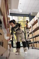 Warehouse manager scanning cardboard box barcode using store scanner, working at merchandise shipping for customers. Supervisor wearing headphones listening music during storehouse inventory photo