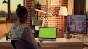 Teleworker using greenscreen on laptop while working remotely on freelance job, looking at copyspace template on device screen. African american woman works with isolated chroma key. photo