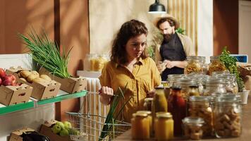 vegano mujer en especialidad cero residuos supermercado oliendo abultar artículos antes de agregando ellos a compras cesta. cliente en local barrio tienda pruebas a ver Si comida es toxinas gratis antes de comprando eso foto