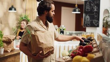 Vegan man in zero waste supermarket using biodegradable paper bag while shopping for bio vegetables. Customer in carbon neutral local grocery shop with no single use plastics policy photo