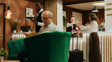 Old woman filling in registration forms at front desk, passing room check in and preparing to start retirement vacation trip. Traveller asking receptionist about all inclusive service. Handheld shot. photo