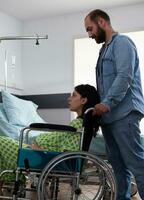 Pregnant woman sitting in wheelchair while future father taking her to maternity room preparing for child delivery in hospital ward. Young couple getting ready for childbirth, discussing parenthood photo