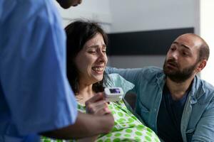 Nurse and husband comforting pregnant patient in hospital ward, having painful contractions. Womana with pregnancy getting into labor having medical assistance during checkup visit. Close up photo