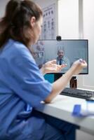 Nurse at desk in telemedicine videocall communicating with doctor specialist in professional medical office. Medic having online internet video conference with young colleague photo