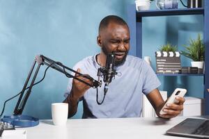 Confused vlogger reading negative feedback from subscriber on smartphone and broadcasting online. Frustrated blogger sharing bad news while creating web content for podcast photo