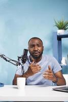 African american blogger speaking in microphone while streaming online on web channel. Young man vlogger talking with subscribers while creating digital content and recording video portrait photo