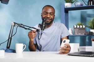 Cheerful blogger sharing insights and news from smartphone while streaming online. Smiling african american vlogger creating digital content and answering question on mobile phone photo