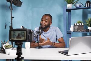 Blogger looking at professional camera while filming digital content for internet channel. Web content creator speaking while streaming and using vlogging equipment in home studio photo