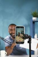 africano americano blogger demostración regalar regalo caja en teléfono inteligente pantalla de cerca. vlogger promoviendo producto mientras anunciando en línea concurso con premio y transmisión utilizando móvil teléfono foto