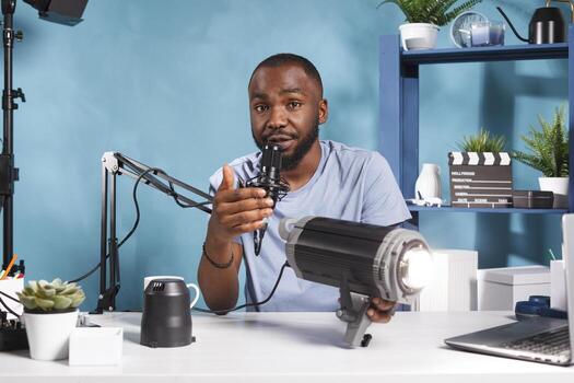 Blogger talking about studio lightning gear in microphone and showing product to subscribers. Internet influencer reviewing videography tool while live streaming and looking at camera photo