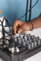 Man arm turning knob cap on volume controller in blogger studio close up. African american vlogger using sound mixer station professional equipment while creating web content photo