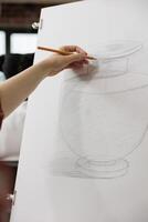 Woman student or art school drawing realistic vase in pencil, sketching on paper during lesson, learning pencil shading techniques. People learn to draw to train creativity in adulthood photo