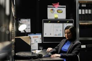 Businesswoman packing laptop up in office suitcase bag preparing to clock out and leave work. Asian bookkeeping employee in business accountancy company file cabinet repository photo