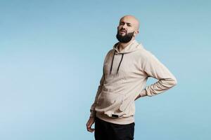 Arab man with lower back injury and looking at camera with painful facial expression. Grimacing young person suffering from backache and holding hand on sore muscles portrait photo