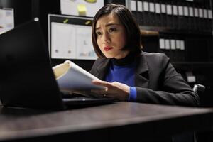 Wheelchair user checking annual profit revenue paperwork before business meeting. Asian executive with disability doing objective completion measurements in dark file cabinet office photo