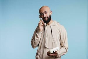 Excited arab man answering call while holding old fashioned landline phone portrait. Young person having conversation on retro telephone and looking at camera with amazed expression photo