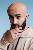 Thoughtful arab man rubbing chin while looking at camera with puzzled facial expression. Pensive arabian person making decision and solving problem with unsure emotions studio portrait photo