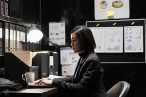 Business invoicing management executive asian woman imputing accountancy market data analysis paperwork on laptop. Archival repository with folders in cabinet and flowcharts photo