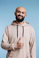 Young cheerful arab man with satisfied smile showing thumb up gesture portrait. Smiling arabian person confirming agreement while looking at camera with carefree face expression photo