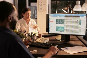 Broker analyzing stock market investment revenue data on computer screen in coworking space, checking company financial statistics. Employee monitoring invested funds in office at night photo