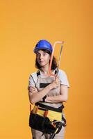 Woman professional carpenter using saw to work on renovating project, doing refurbishment work in studio. Builder holding handsaw with razor blade, wearing overalls and protective helmet. photo