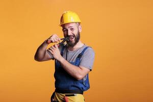 Male restore expert using pair of pliers to repair, working as carpenter or constructor in studio. Professional construction worker with hardhat holding pliers and renovating tools on background. photo