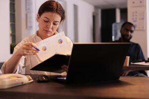 Financial analyst reading company report, analyzing statistics data, project manager planning startup strategy. Employee checking research result at workplace desk in coworking space photo