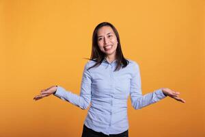 Doubtful filipino woman being hesitant and unconfident while trying to answering question. Confused and clueless model shrugging shoulders having uncertain expression in studio over yellow background photo