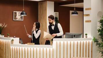 Teamworking professional receptionists checking guests vacation packages at check in reception desk. Hotel personnel booking incoming tourists, working in stylish resort lounge photo