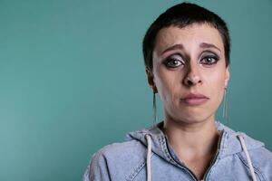 Portrait of depressed unhappy caucasian female looking at camera while crying in studio with isolated background, person having mental breakdown. Worried woman with grief expression photo