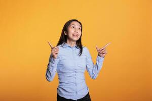 exitoso filipino modelo señalando dedo arriba posando en estudio en amarillo antecedentes. confidente positivo mujer publicidad rebaja producto, demostración anuncio icono o ejemplo en cámara. anuncio concepto foto