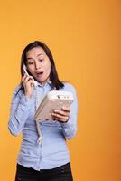 alegre modelo mujer respondiendo teléfono fijo teléfono llamada en estudio, teniendo remoto conversacion con remoto amigo utilizando teléfono con cable. mujer teniendo discusión en teletrabajo comunicación dispositivo. foto