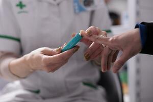 Woman measuring blood sugar level for diabetes screening in apothecary. Pharmacy employee using glucometer in pharmaceutical store, pressing client finger to medical device close up photo