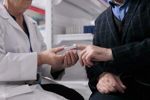 Pharmaceutical employee measuring customer oxygen saturation and giving healthcare consultation in apothecary. Elderly man holding pulse oximeter medical instrument on fingertip photo