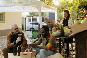 Young African American guy customer tasting homemade natural wine while sitting at table with winemaker at farmers market. Consumer sampling local produce while visiting organic food festival photo