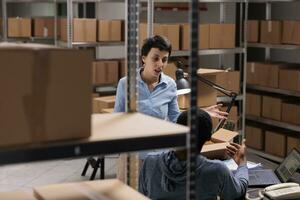 Diverse warehouse employees discussing transportation logistics problem while preparing customer packages, working in storehouse delivery department. Workers preparing online orders photo