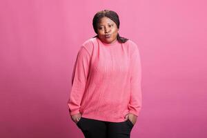 Portrait of doubtful woman shrugging shoulders having questioning facial expression, standing over pink background. Thoughtful adult standing with hands spread wide, pensive person looking at camera photo