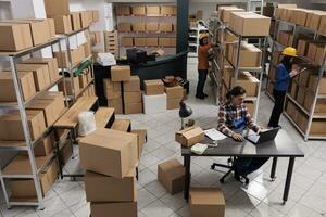 Asian postal service team doing inventory in industrial warehouse. Storehouse man and women employees checking cardboard boxes storing, managing logistics and distribution top view photo