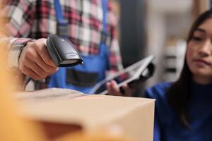 Freight distribution center employee using barcode scanner in warehouse. Logistic manager scanning cardboard box qr code while supervising goods receiving and sending operations photo