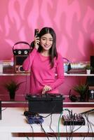 Dj artist performing techno music in club at night using professional turntables, having fun with fans during concert. Asian performer with pink blouse mixing electronic sounds in studio photo