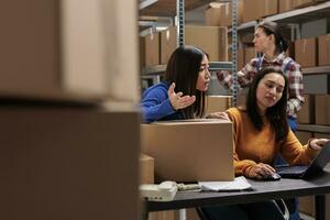 Postal warehouse employees checking delivery compliance and planning logistics on laptop. Young asian women order pickers discussing customer pick ticket on computer in storehouse photo