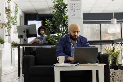 Arab business entrepreneur working at marketing data management on laptop in open space modern office. Start up executive manager solving job task while typing on computer photo