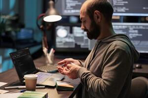 IT engineer taking vitamins and working after hours, using medicine and supplements to stop being tired or stressed. Taking medicaments from foil and box, programming source code. photo